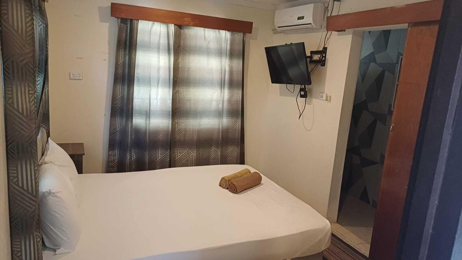 Ein Hotelzimmer mit einem Bett, einem an der Wand montierten Fernseher und einem Fenster mit gemusterten Vorhängen.