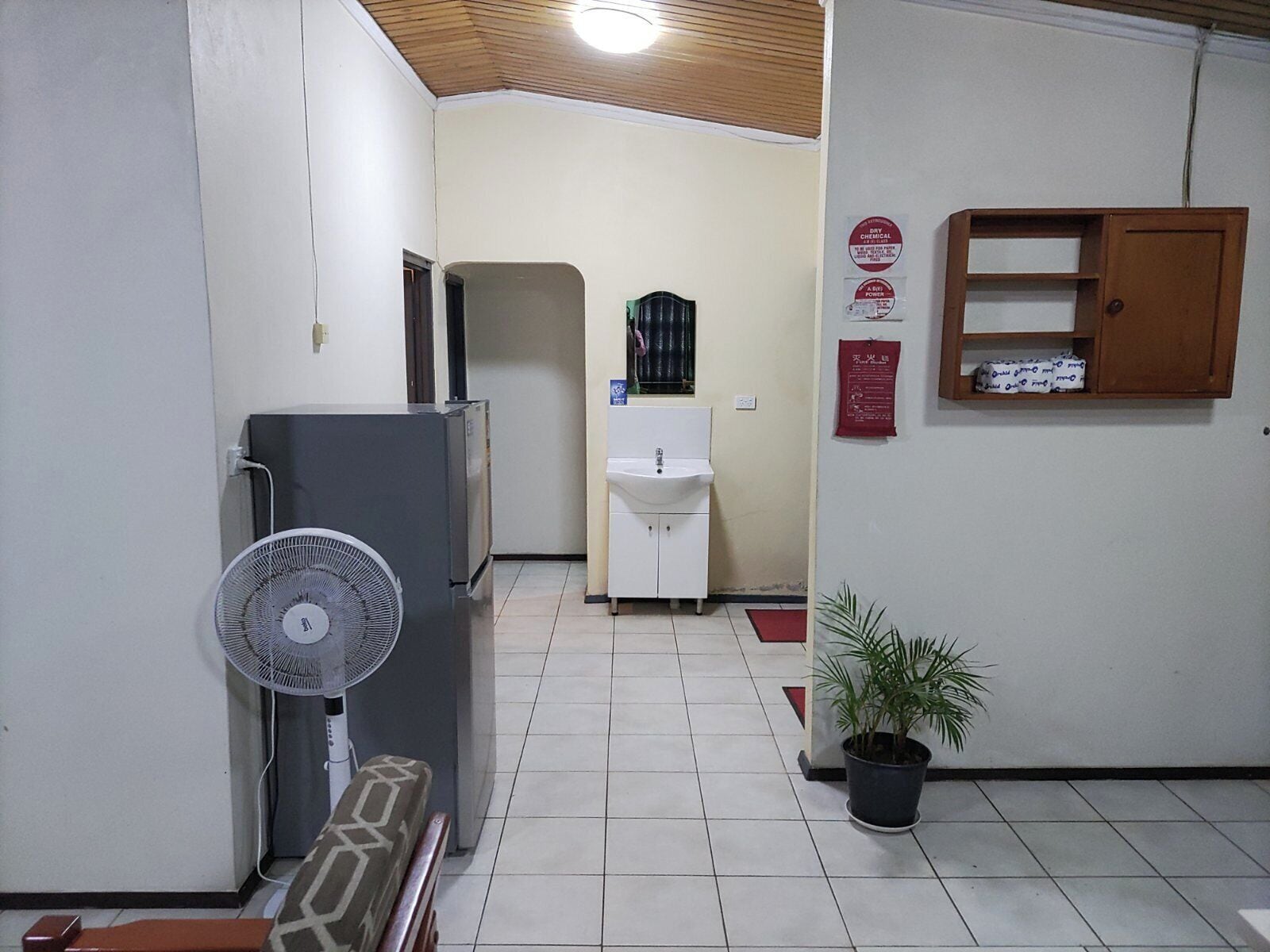 Un pasillo estrecho con un refrigerador, un lavamanos, un ventilador y un armario de madera.