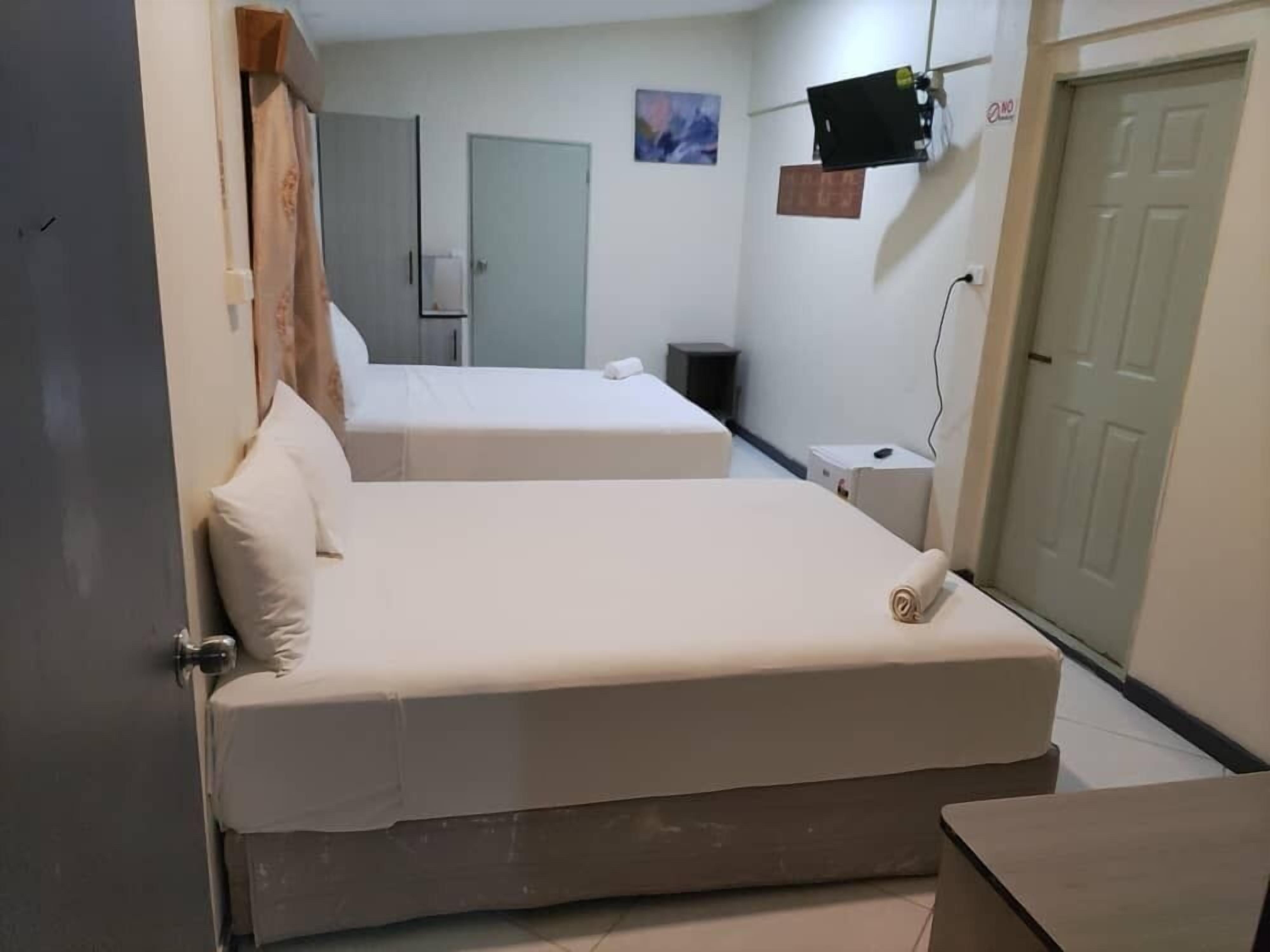 Une chambre avec deux lits, une porte, un téléviseur et un tableau au mur.