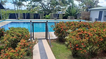 A swimming pool with a gated entrance, surrounded by lush greenery and flowering bushes.