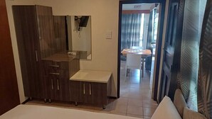 A bedroom with a wardrobe, a bedside table, and a mirror. There is a door leading to a dining area with a table and chairs. - Bula Retreat (Sigatoka)