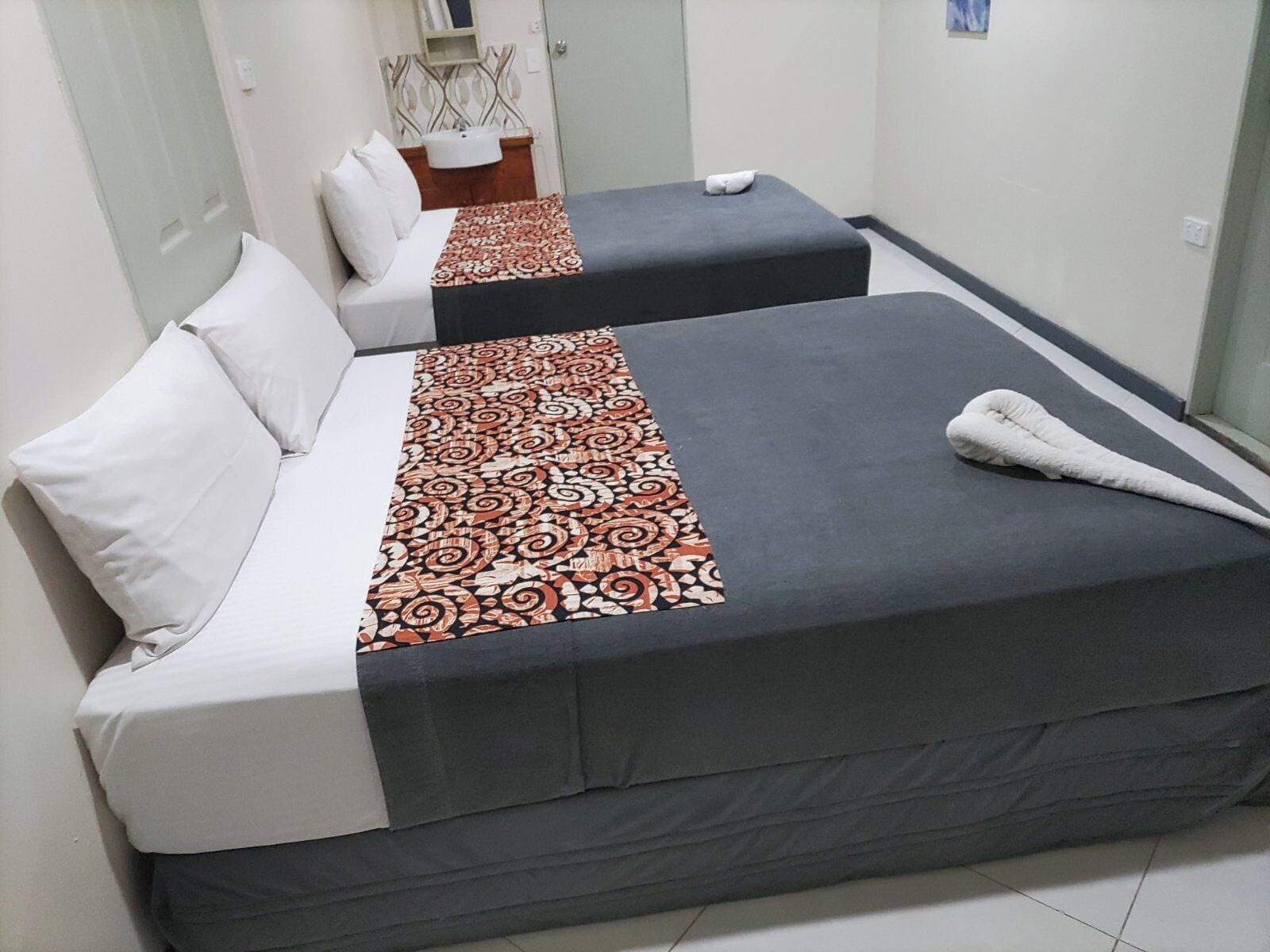 Two single beds with patterned bedspreads, a white pillow, and a white towel on the floor.