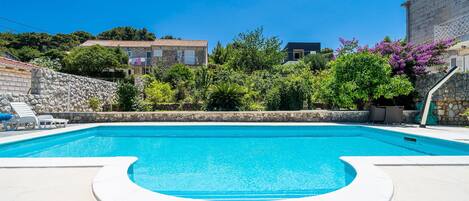 A swimming pool with a stone wall and greenery around.