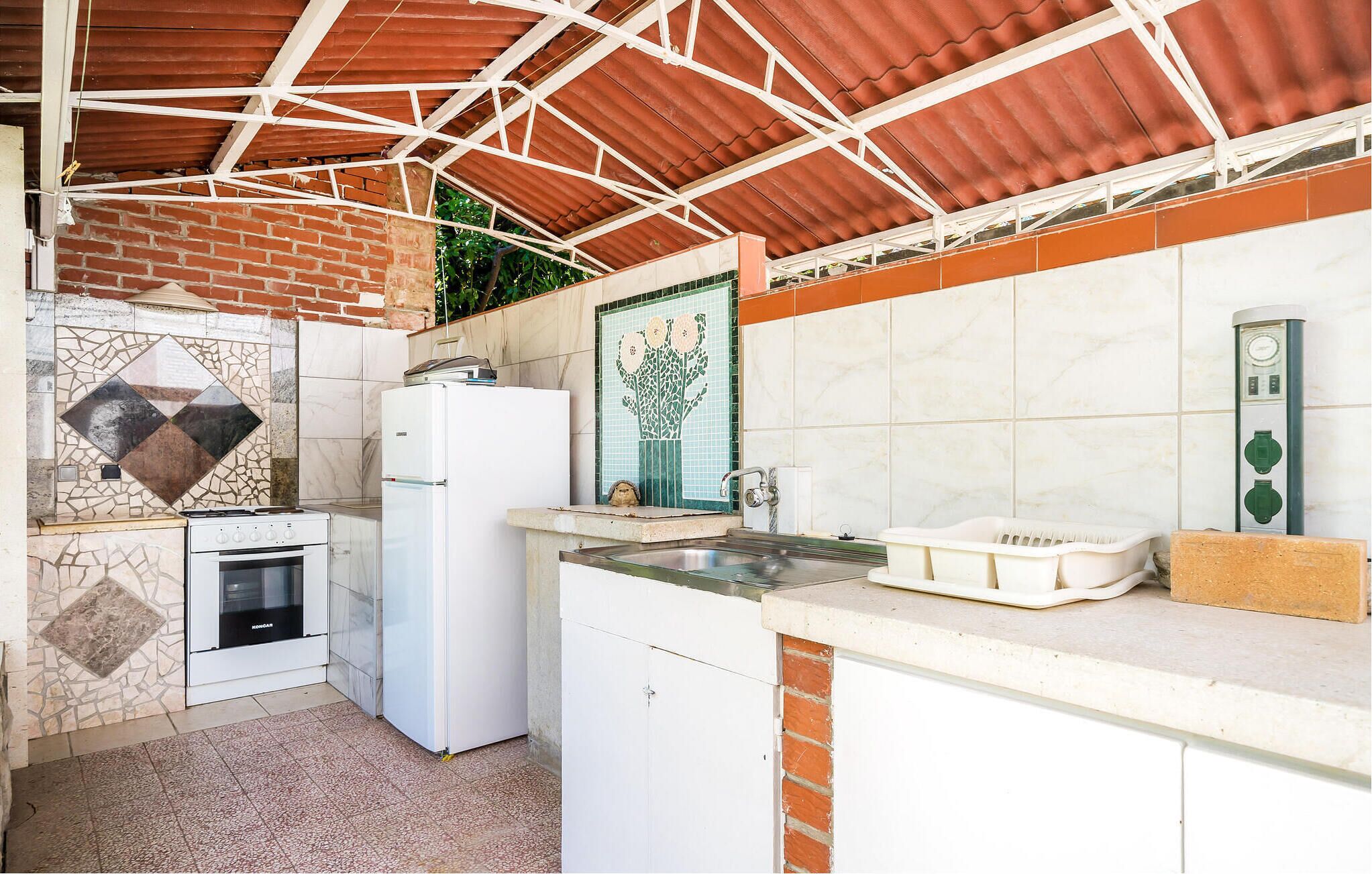 Una cocina compacta con estufa a gas, refrigerador, pileta y salpicadero de azulejos.