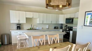 A modern kitchen with white cabinets, a wooden dining table, and a stainless steel trash can. - Mama Lou's Hide-A-Way   (Rainbow Bay)