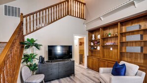 A living room with a staircase, a flat-screen TV, a grey sofa, a blue pillow, and wooden shelving. - 4 Bedroom & Pool: Great Irving Location close to attractions (Irving)