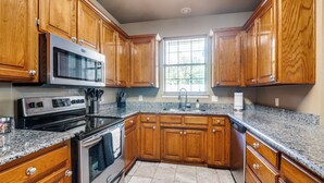 A kitchen with wooden cabinets, a stainless steel oven, a microwave, granite countertops, and a window with a view of trees. - 4 Bedroom & Pool: Great Irving Location close to attractions (Irving)