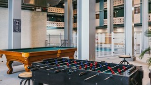 Een pooltafel en een tafelvoetbaltafel in de hotellobby, met uitzicht op balkons en een witte hek.