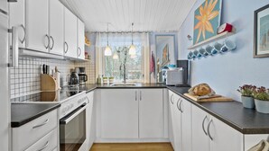 Cocina moderna con armarios blancos, encimera de madera, horno empotrado y ventana con cortinas.