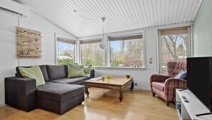 Una sala de estar moderna con un sofá modular, un sillón de cuadros, una mesa de centro de madera y ventanas amplias con vistas al exterior.