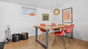 Un comedor con mesa de madera, sillas rojas, una lámpara colgante e impresión enmarcadas en la pared.