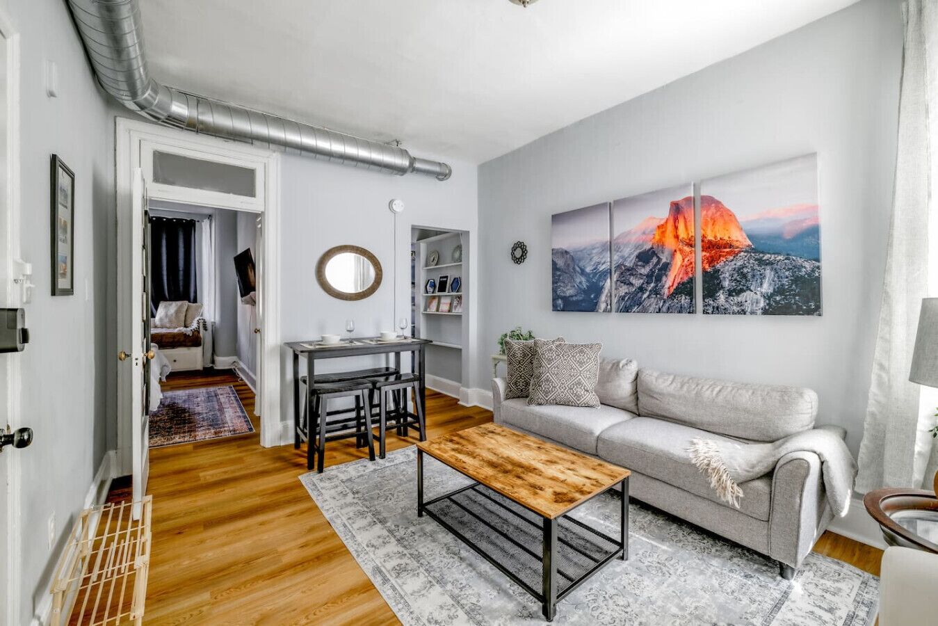 Un salon moderne avec une table basse en bois, un canapé gris et un tableau représentant un paysage de montagne.