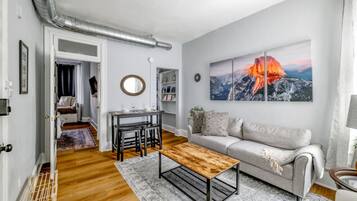 Un salon moderne avec une table basse en bois, un canapé gris et un tableau représentant un paysage de montagne.
