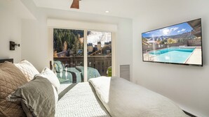 Ein Schlafzimmer mit Bett, Deckenventilator, großem Fenster und Fernseher, der einen Blick auf einen Pool zeigt.