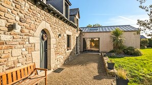 A stone building with a wooden bench, a gravel pathway, and a modern structure with a metal roof. - Gorgeous home in Quessoy with WiFi (Quessoy)
