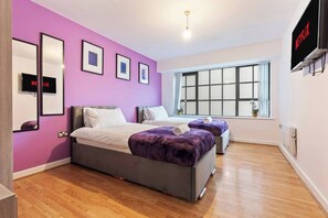 A modern bedroom with a purple wall, two beds, a large window, and a TV displaying 'NETFLIX'.