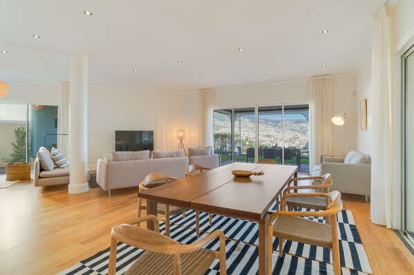 A modern living room with a large dining table, sofas, and a TV. - Sublime View Villa by Atlantic Holiday (Funchal)