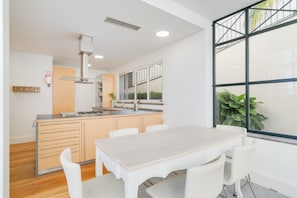 A modern kitchen with a central island, white cabinetry, and a large window with a view of greenery. - Sublime View Villa by Atlantic Holiday (Funchal)