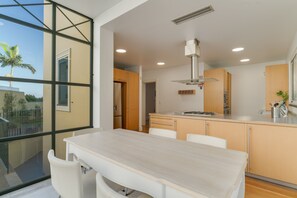 Una cocina moderna con un amplio ventanal, armarios de madera y una mesa de comedor blanca.