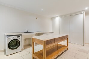 A modern kitchen with a built-in washing machine, a wooden table, and a white countertop. - Sublime View Villa by Atlantic Holiday (Funchal)