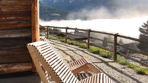 Una panca di legno con vista su un paesaggio montuoso, delimitato da una recinzione di legno.