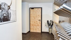 Un corridoio con una porta in legno, un quadro appeso al muro, un vaso con piume e una ringhiera metallica per le scale.
