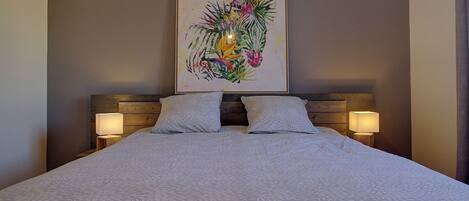 Una cama bien hecha con una colcha estampada, dos almohadas y un cabecero con una obra de arte enmarcada. Hay dos lámparas de noche sobre mesitas de madera.