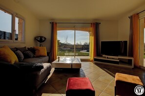 Ein Wohnzimmer mit einer Couch, einem Couchtisch, einem Fernseher und einer Glastür, die auf einen Balkon führt.