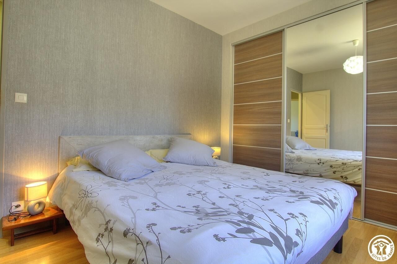 Un dormitorio con cama, lámparas de noche, mesita de noche y armario con espejo.
