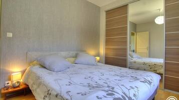 Un dormitorio con cama, lámparas de noche, mesita de noche y armario con espejo.