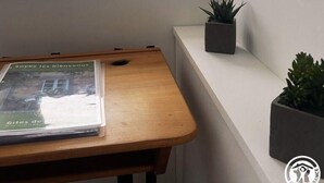 A room with a window, a wooden table, a potted plant, and a framed picture on the wall.