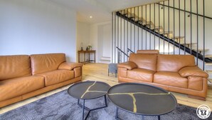 A living room with two brown leather sofas, a coffee table, and a staircase with a metal railing.