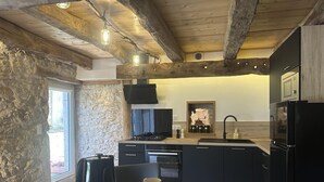 A modern kitchen with a stone wall, wooden beams, and black cabinetry.