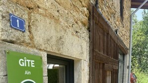 A stone building with a wooden door and a green sign indicating it is a Gîte Ain.