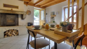 Cocina rústica con chimenea de piedra, vigas de madera y comedor con sillas y una mesa dispuesta para el desayuno.