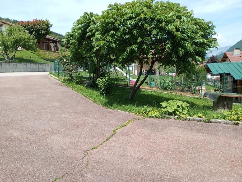 Un sendero pavimentado que conduce a un área verde con un árbol y una valla.