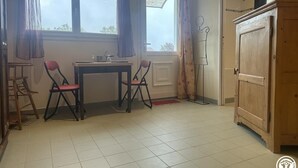 Une pièce comprenant une table à manger, deux chaises, un buffet et une fenêtre avec des rideaux.