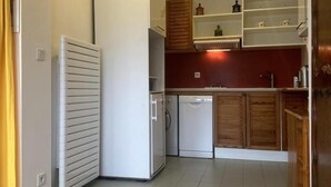 Une cuisine de taille réduite, avec des appareils électroménagers blancs, des armoires en bois et un sol carrelé.