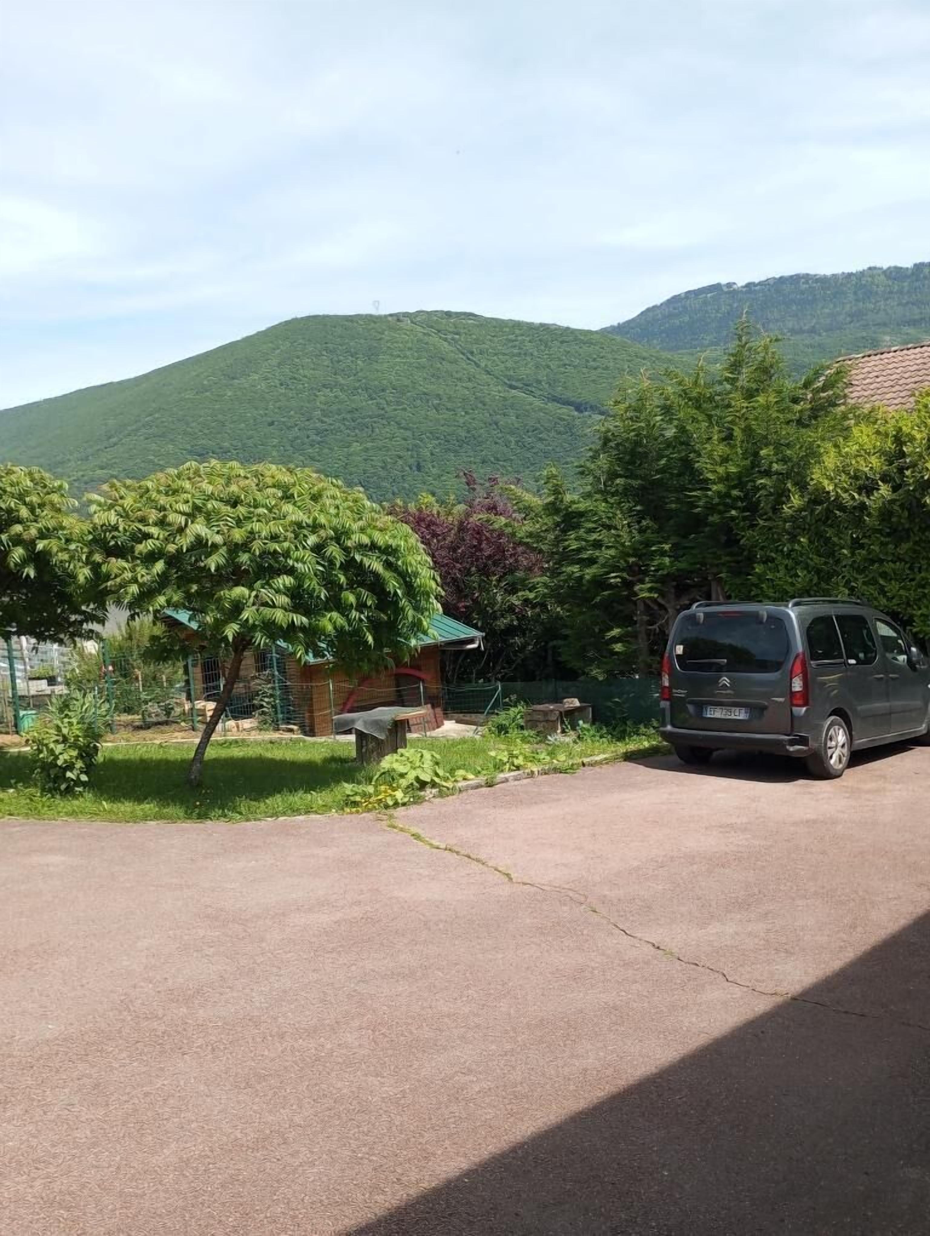 Un estacionamiento con un coche aparcado, un edificio pequeño y una colina al fondo.