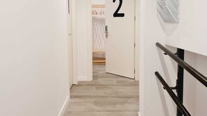 A hallway with a wooden floor, white walls, and a black railing. A door with the number 2 is visible. - Bilbao ROOMS & KITCHEN Irala (Bilbao)
