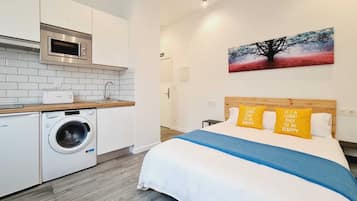 Una habitación de hotel moderna con cama, un cuadro y una kitchenette con lavadora.