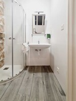 Un bagno con cabina doccia in vetro, un lavandino bianco e uno specchio sopra.