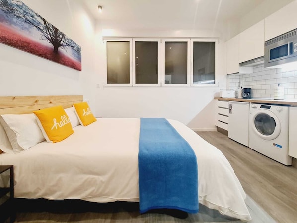 A bedroom with a bed, a washing machine, and a kitchen area. - Bilbao ROOMS & KITCHEN Irala (Bilbao)