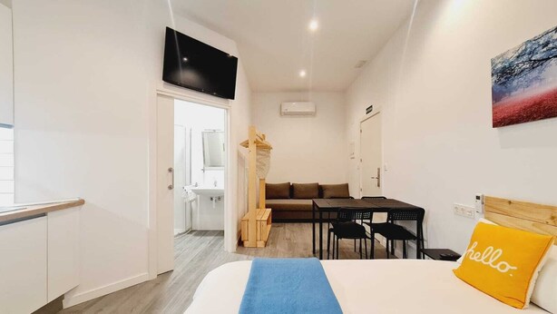 A hotel room with a bed, a desk, a chair, a TV, and a bathroom visible through an open door. - Bilbao ROOMS & KITCHEN Irala (Bilbao)
