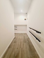 Un corridoio stretto con pavimento in legno e pareti bianche, con un piccolo angolo salotto con una panca e una mensola a parete.