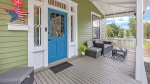 Eine Veranda mit blauer Tür, Sitzgelegenheiten im Freien und einer Willkommensmatte.
