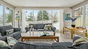 A modern living room with two grey sofas, a wooden coffee table, and a wooden desk with a laptop and books. Large windows offer a view of snow-covered trees. - Nice home in Nykøbing Sj with WiFi (Nykøbing Sj)