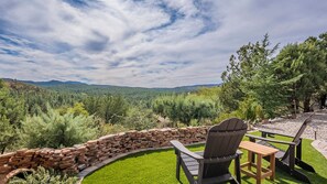 A patio with a stone wall, a wooden table, and a chair overlooking a forested valley.