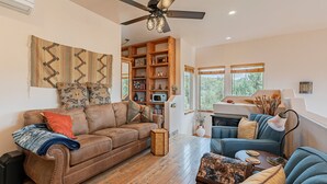 A spacious living room with a brown leather sofa, a blue sofa, and a wooden coffee table. There is a bookshelf filled with books and decorative items, and a fireplace with a mantel.