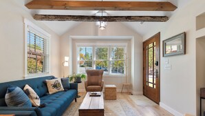 A cozy living room with a blue sofa, a wooden coffee table, and a large window with blinds. - Cozy Cottage across the street from Carl Sandburg National Park (Flat Rock)